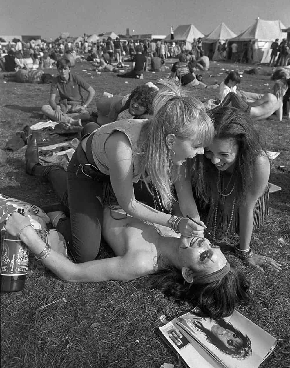 Two girls laughing while drawing on a boys face to make him look like Alice Cooper