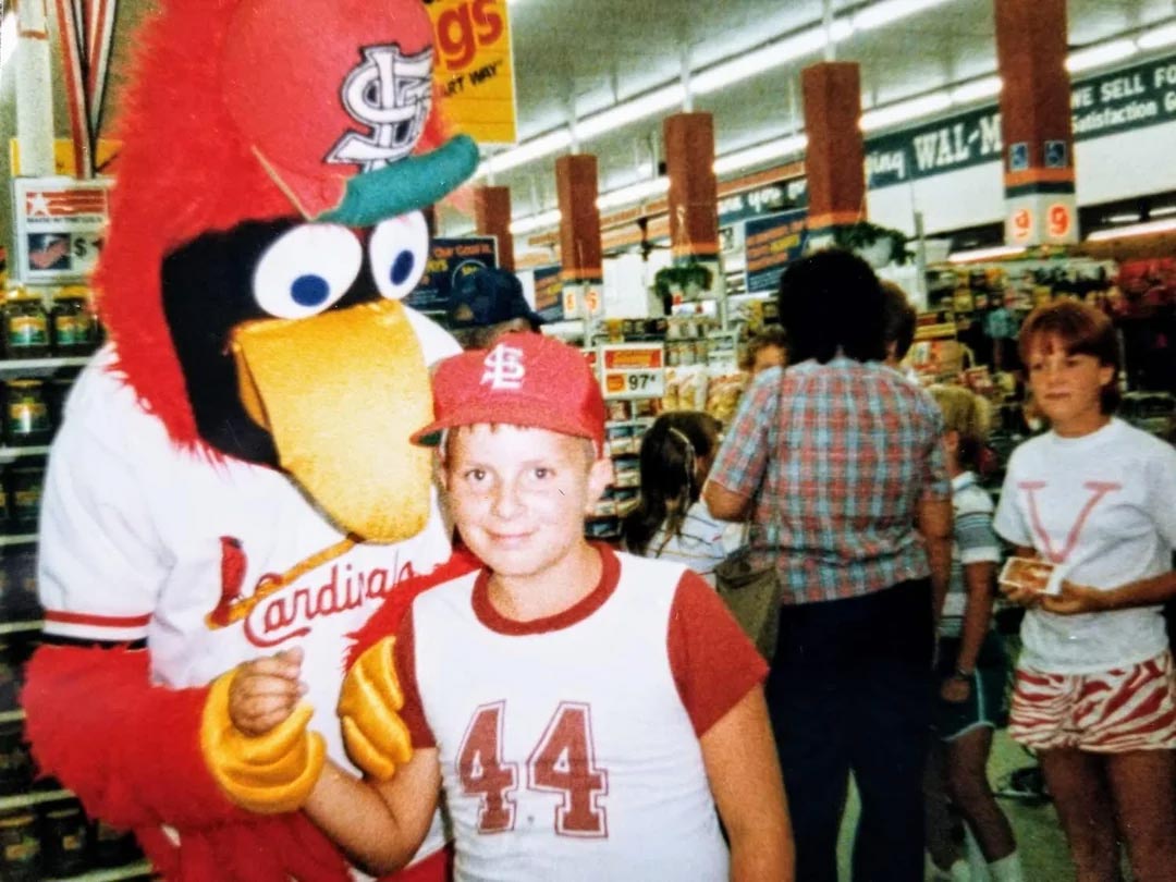 Kid at a grocery store wearing Cardinals gear is posing for a photo with Freebird
