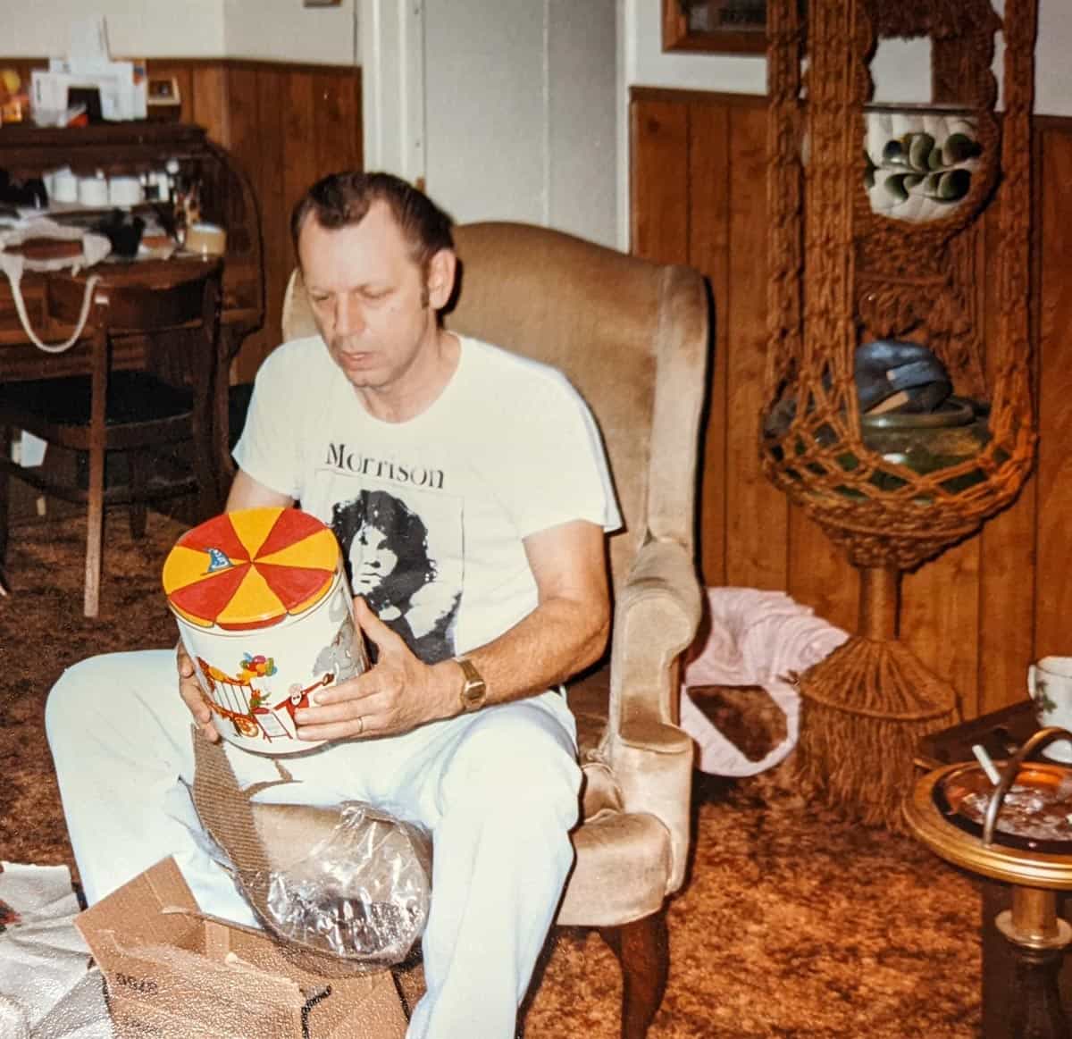 A man sitting in his chair wearing a Jim Morrison shirt looking at a present