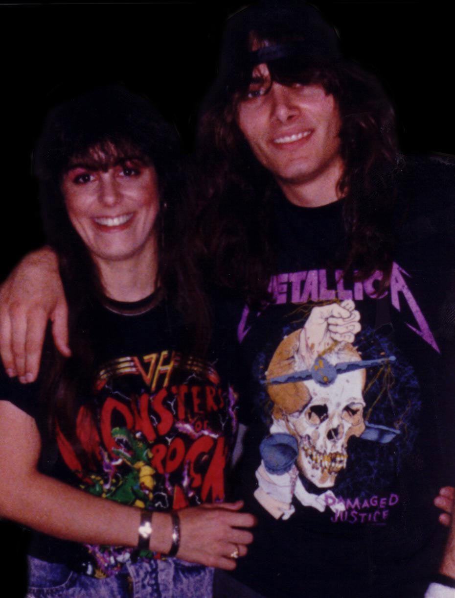 A smiling couple with long dark hair pose together, wearing concert t-shirts — a Van Halen Monsters of Rock shirt and a Metallica Damaged Justice shirt.