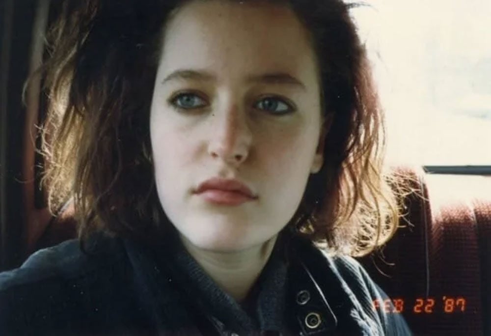 A young woman with dark tousled hair and blue eyes looks directly into the camera in a close-up photo taken inside a vehicle, dated February 22, 1987 in the corner.