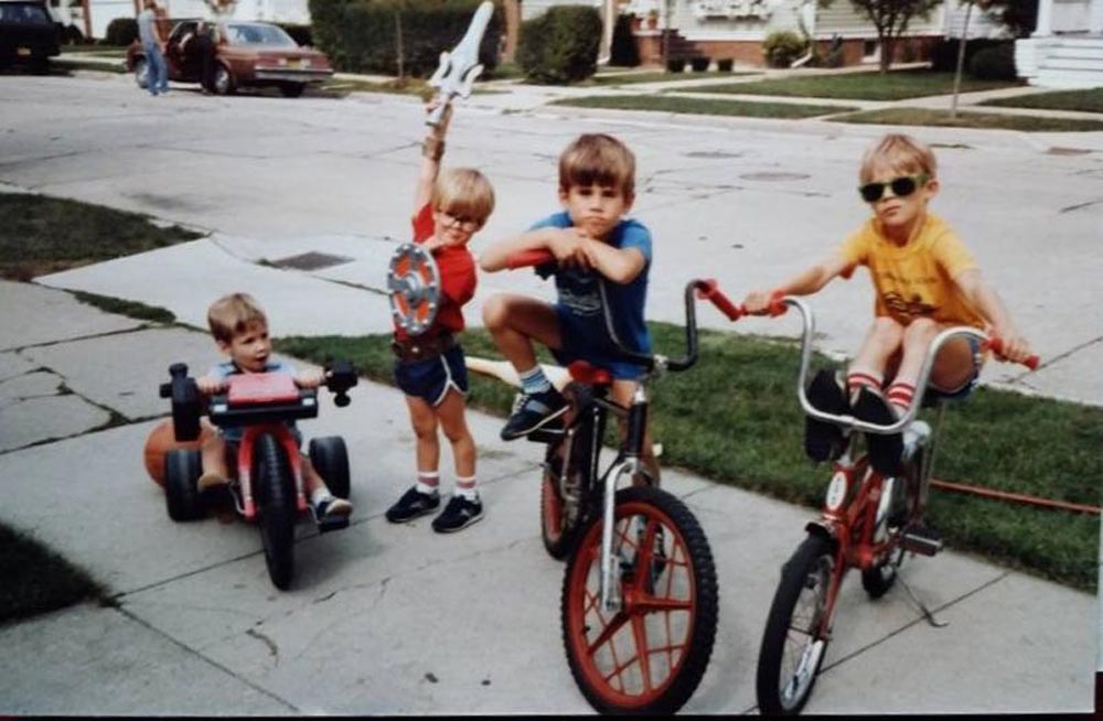 Four kids on the sidewalk hanging out and posing for a photo