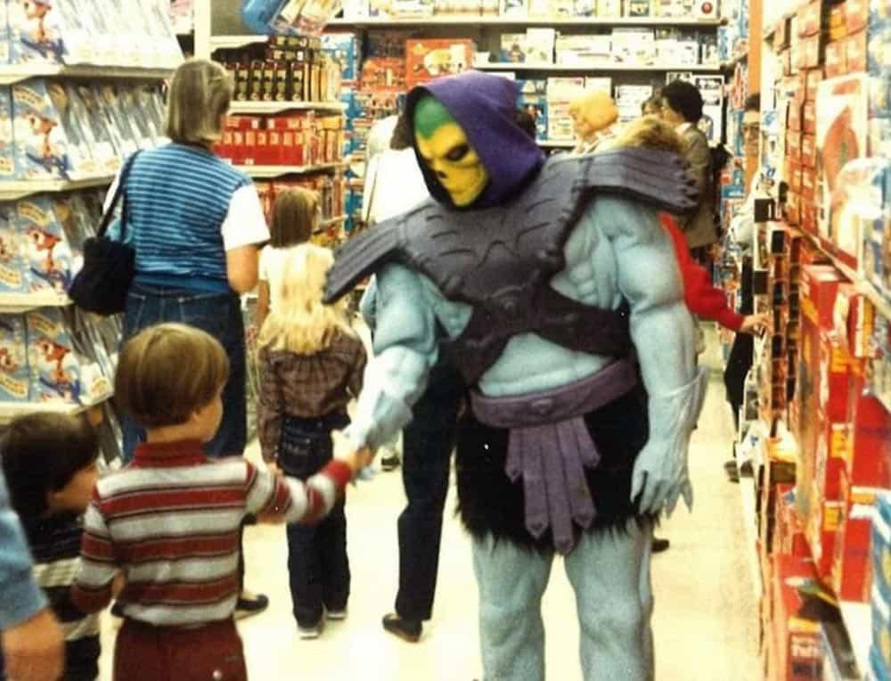 Someone dressed as Skeletor shaking hands with a kid in a aisle of a Toys R Us