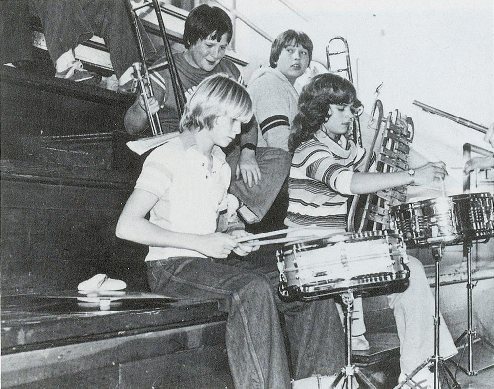 Black and white photo of kids playing music on the bleachers in a gym