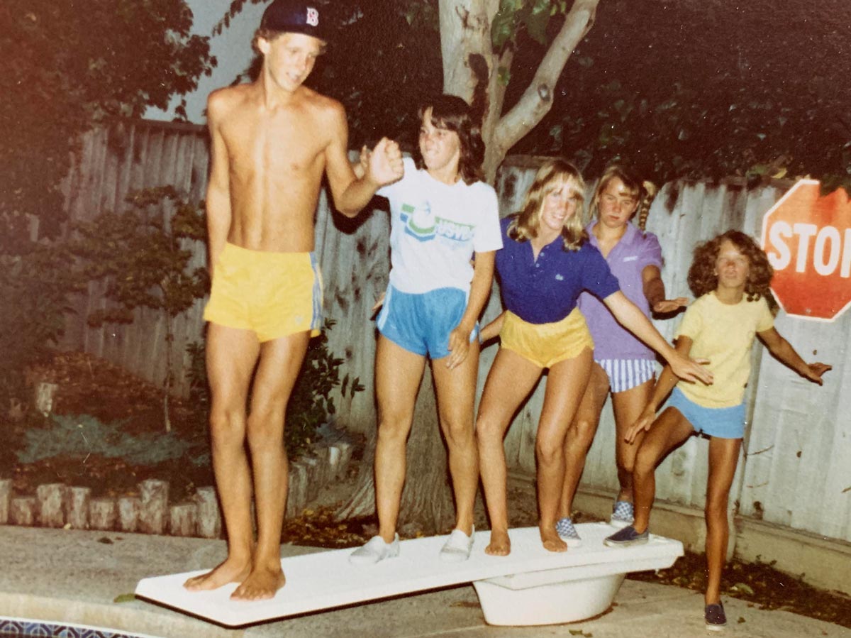 5 teens pose for a photo on a diving board next to a pool