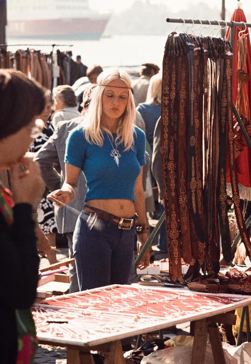 A young woman spinning a necklace while selling leather belts in the 1970s