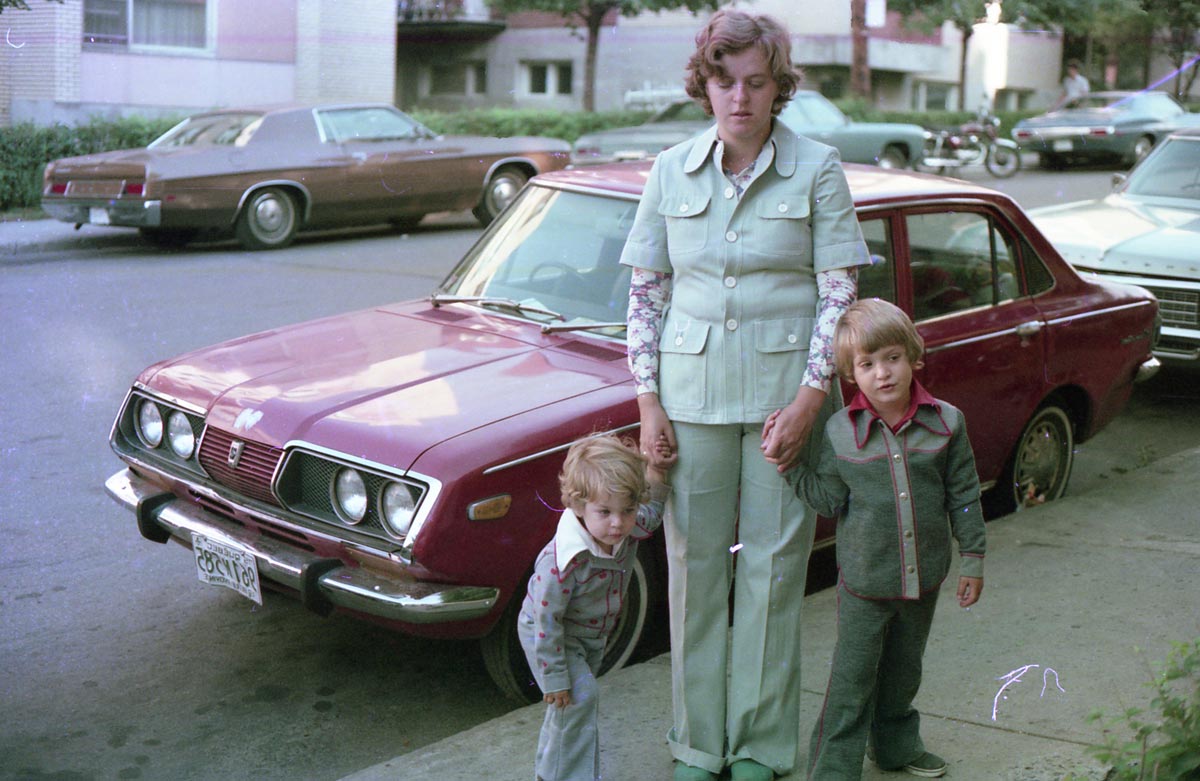 Two kids with their mother on the sidewalk dressed in very 1970s clothes