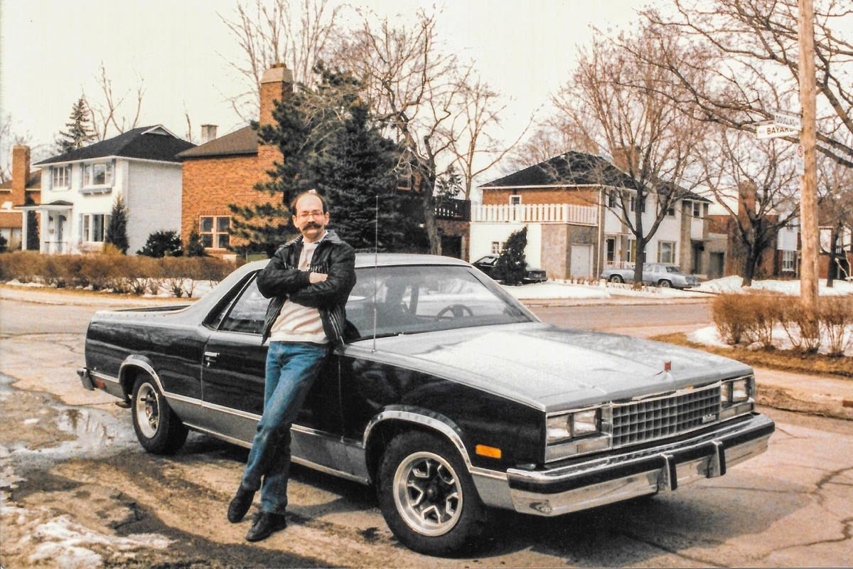 Photo of a mustached man leaning against an El Camino