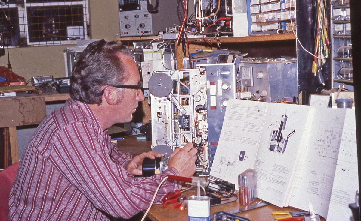 A man looking at an owners manual while trying to repair an electronic device