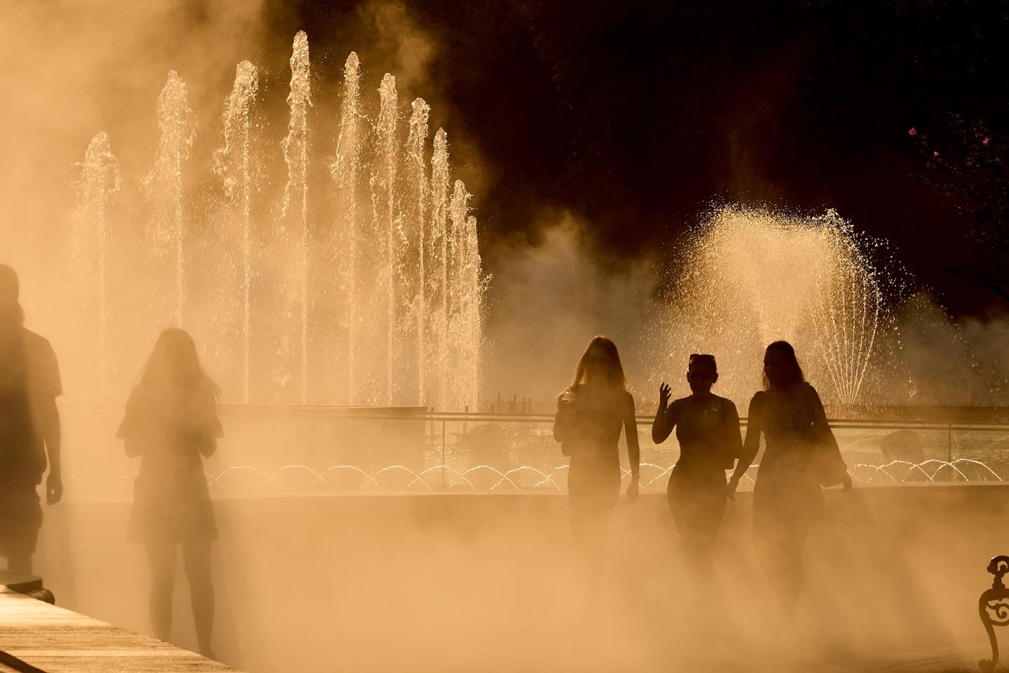 People walk through the fine spray of a fountain in the heat of the summer.