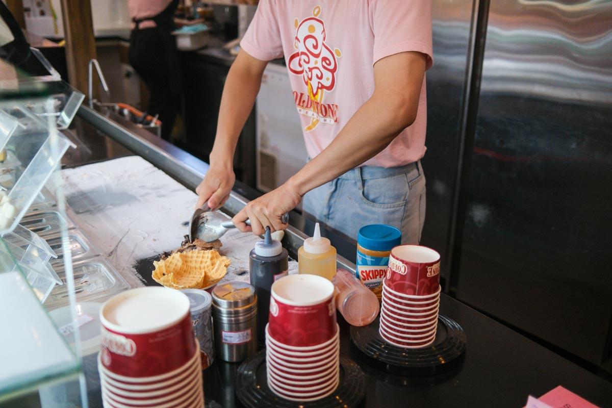 Cold Stone Creamery cups in multiple sizes with ice cream preparation going on behind them