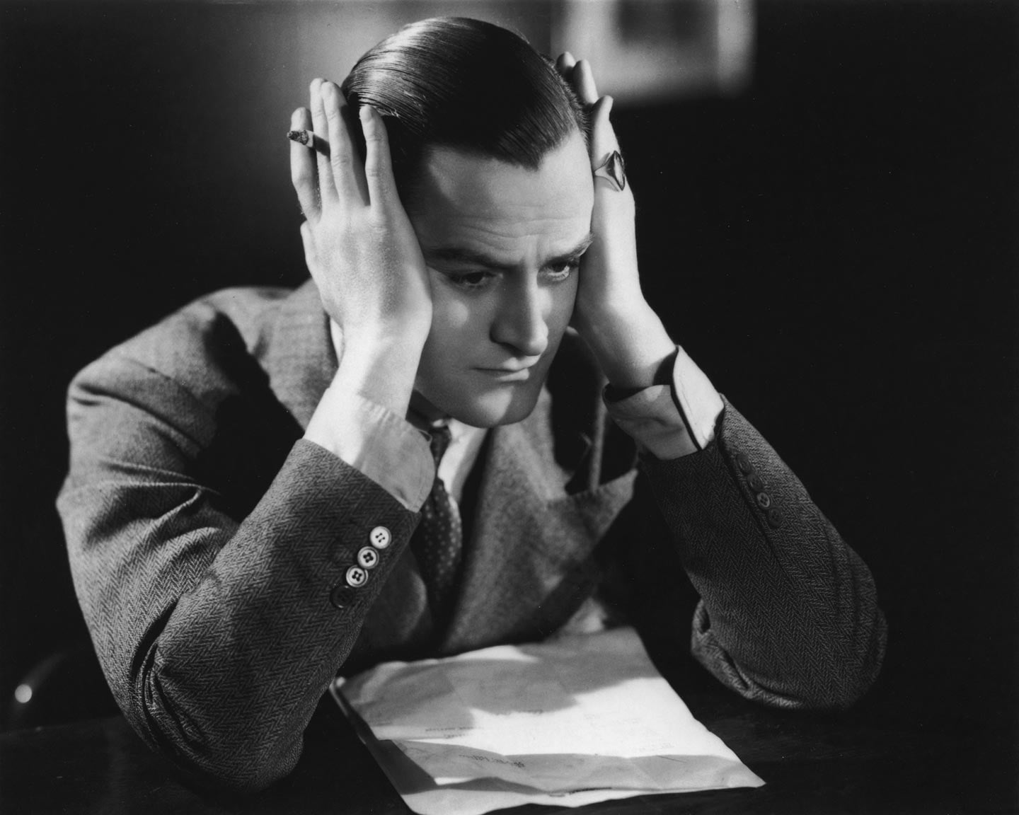 A man resting his head in his hands as he contemplates a letter on the desk in front of him, circa 1935.