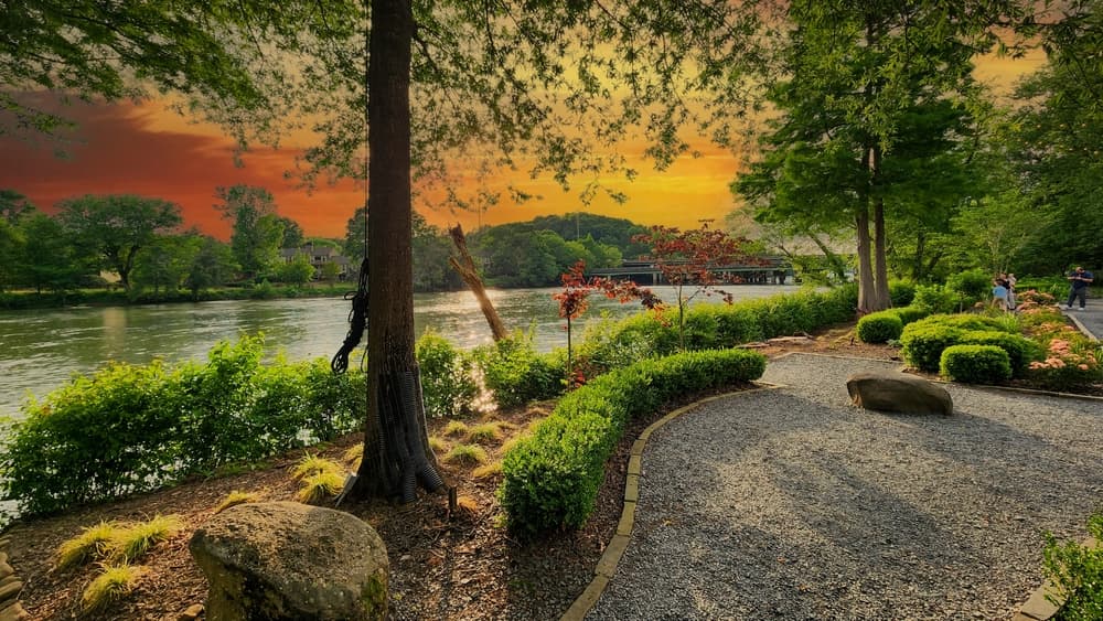 A gorgeous spring landscape along the Chattahoochee River with lush green trees, grass and plants and colorful flowers with powerful clouds at sunset at Ray’s on the River in Sandy Springs Georgia