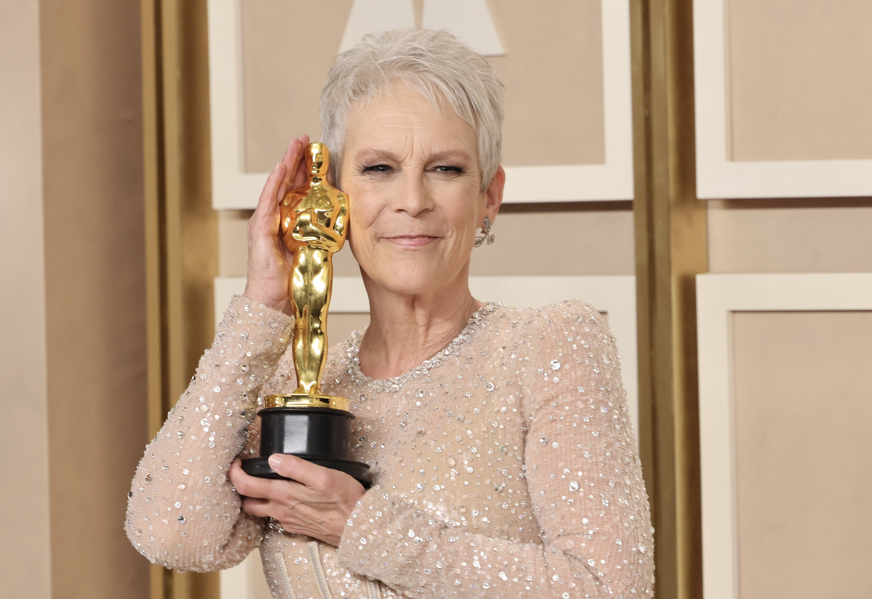 Jamie Lee Curtis in a sparkly gown posing with an Academy Award.