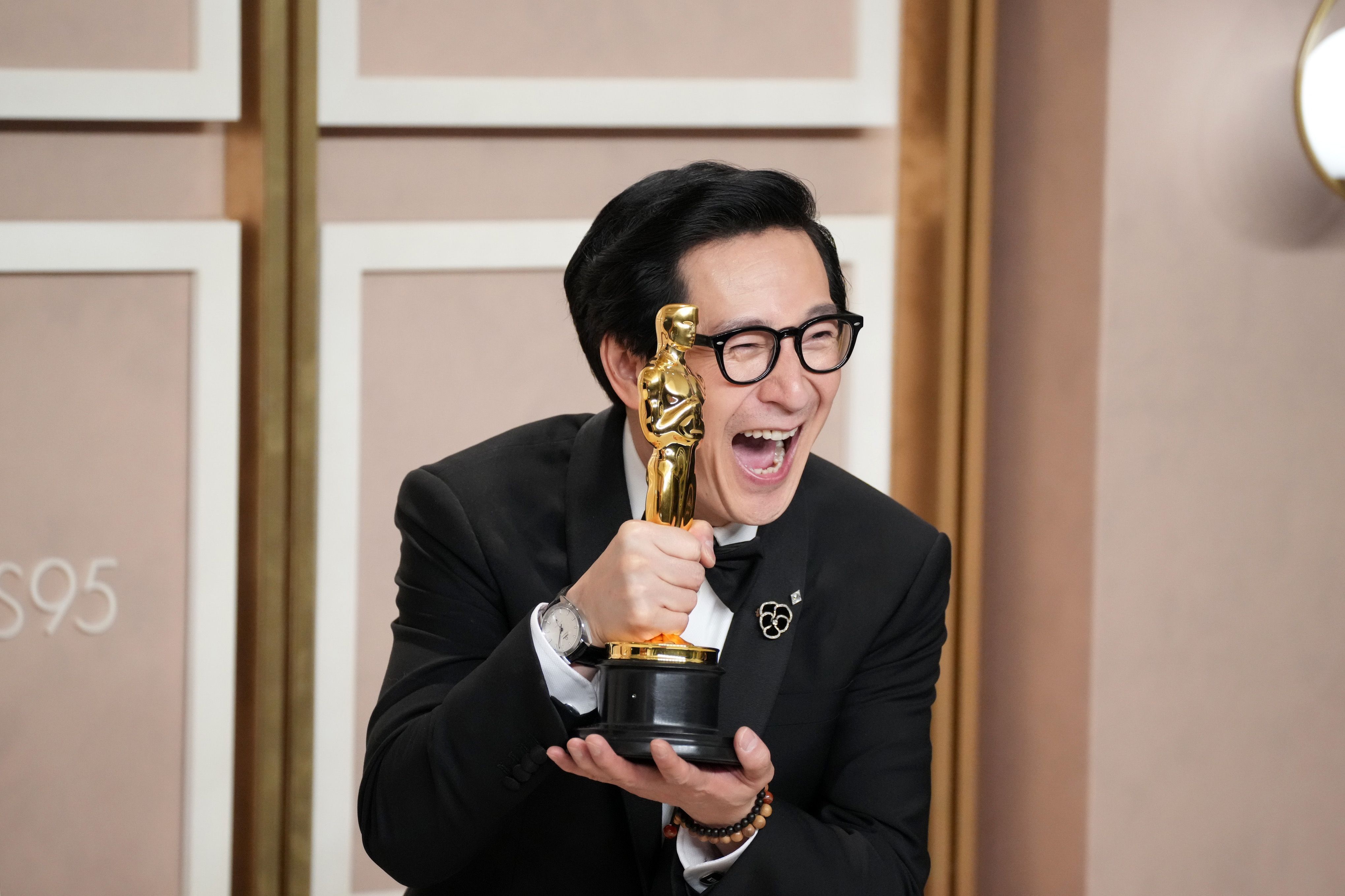 Ke Huy Quan in a black suit smiling with an Academy Award.