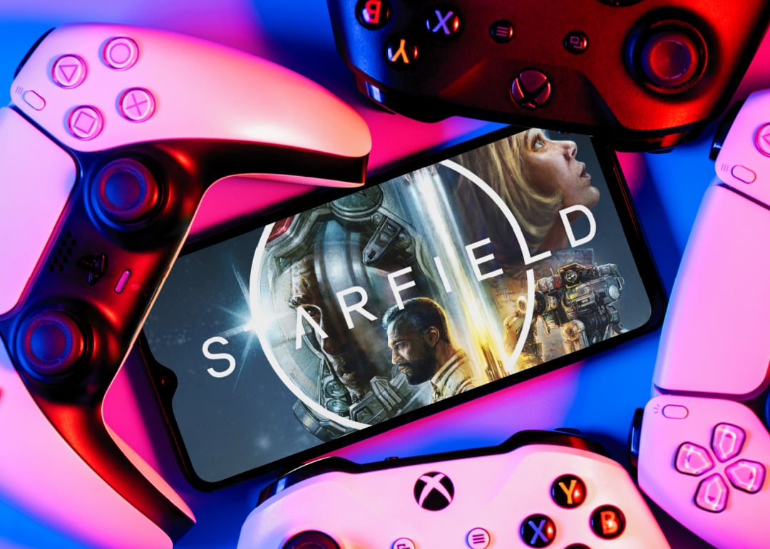 A smartphone with Starfield game logo on screen surrounded by gamepads.