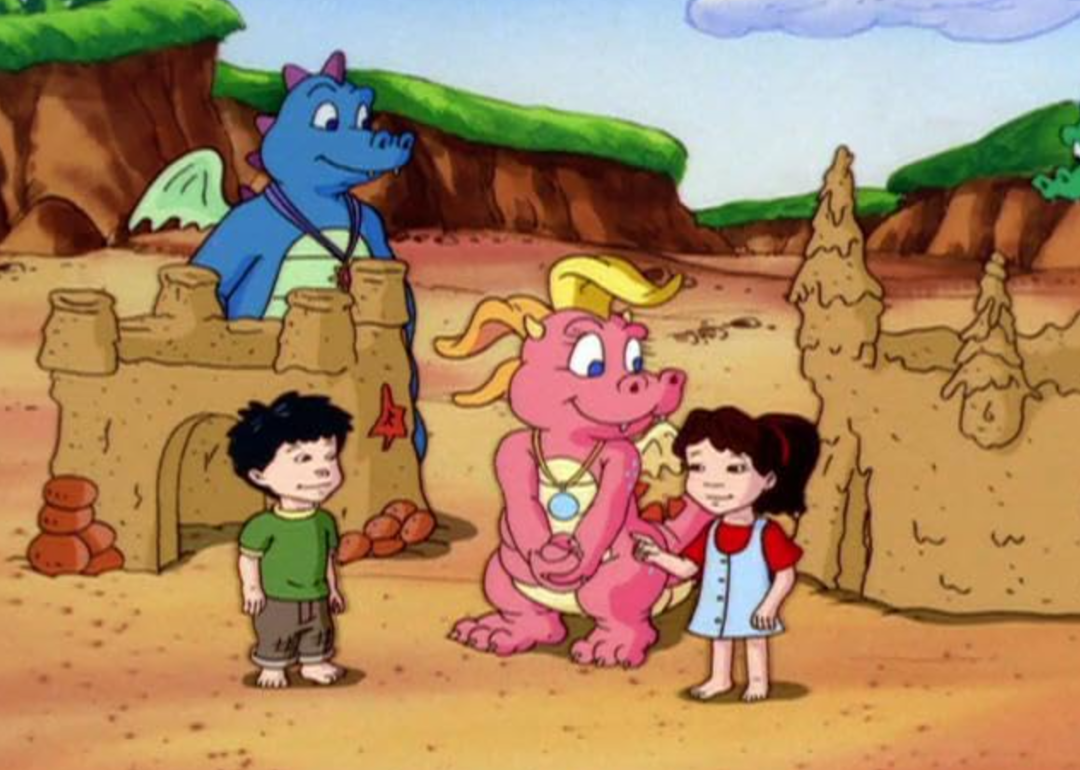 Cartoon of Emmy and Max and two dragons standing next to sandcastles. 