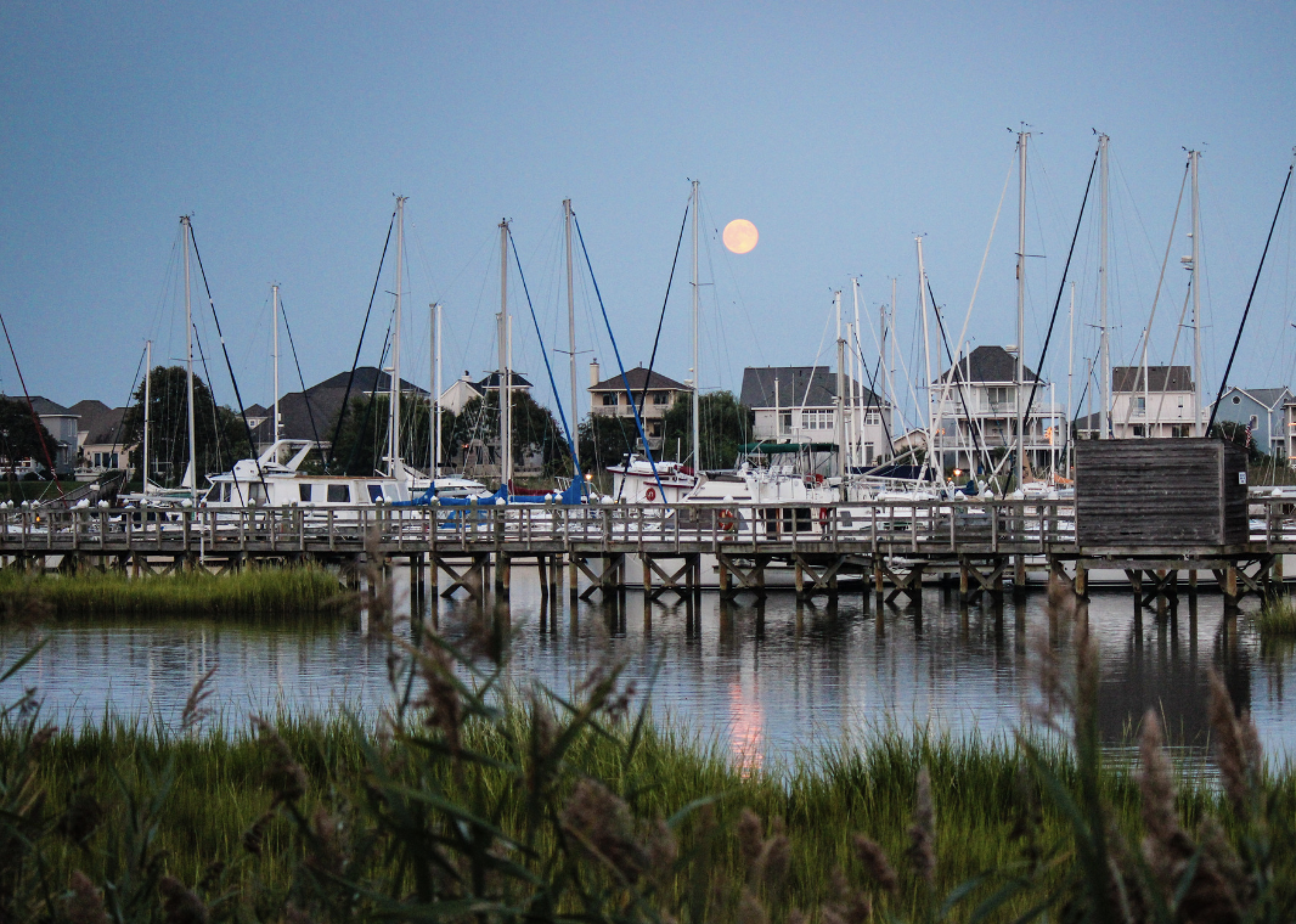A full moon over boats in the harbor.