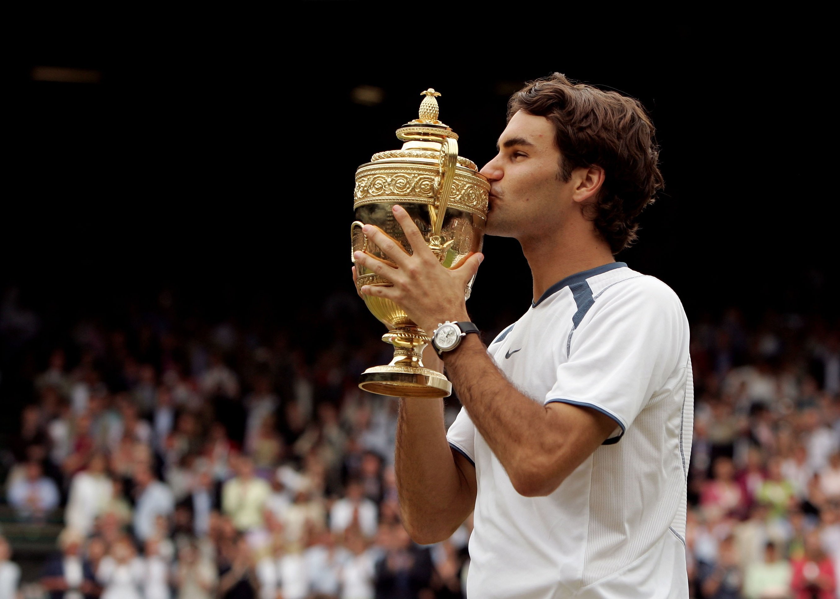Roger Federer celebrates his win by kissing the Wimbledon trophy.