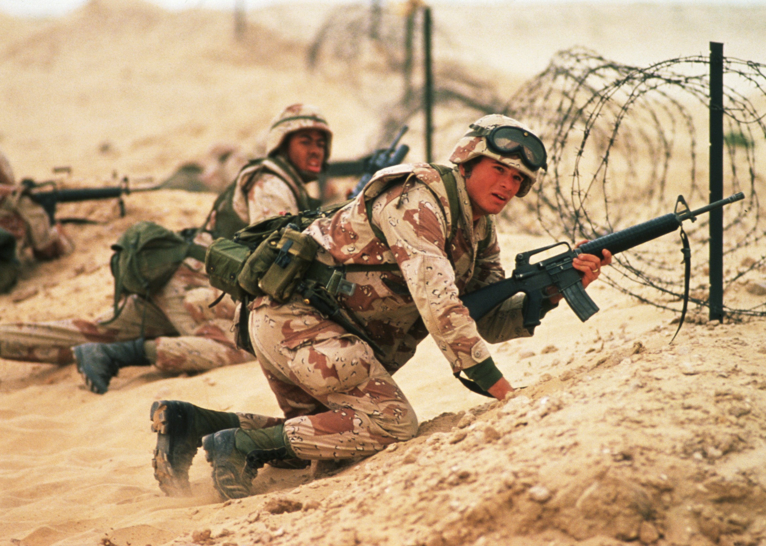 US Marines crouch behind a barrier of barbed wire. 
