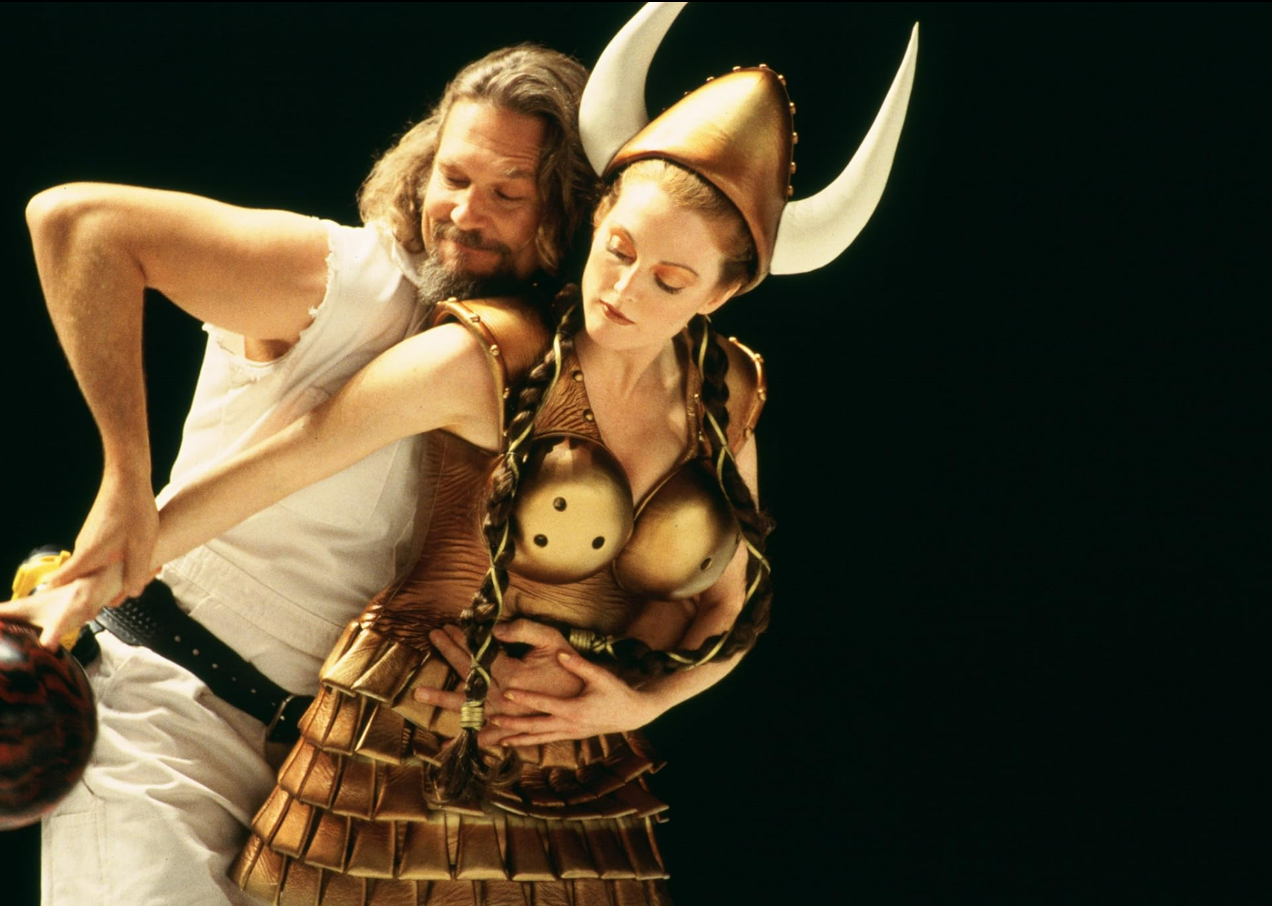 A scene from The Big Lebowski with Jeff Bridges guiding the arm of Julianne Moore who is holding a bowling ball and wearing a viking costume.