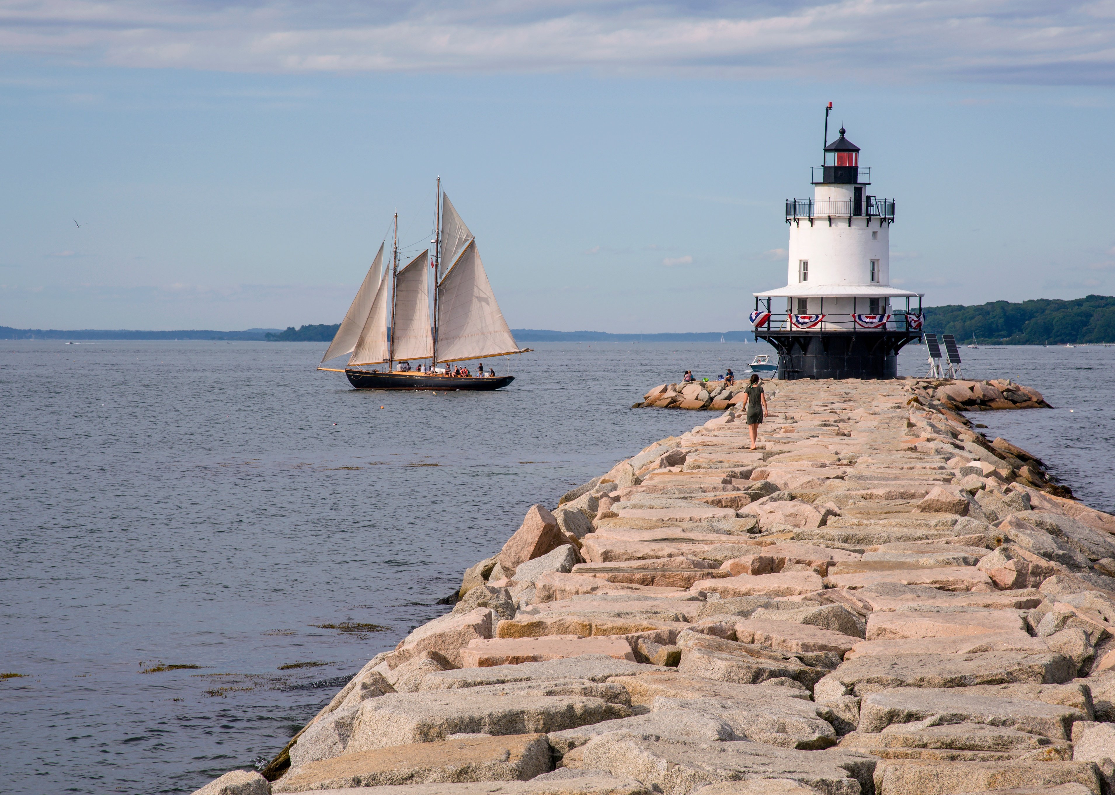 Old schooner sails past Spring Point lighthouse on a summer day in Portland. 