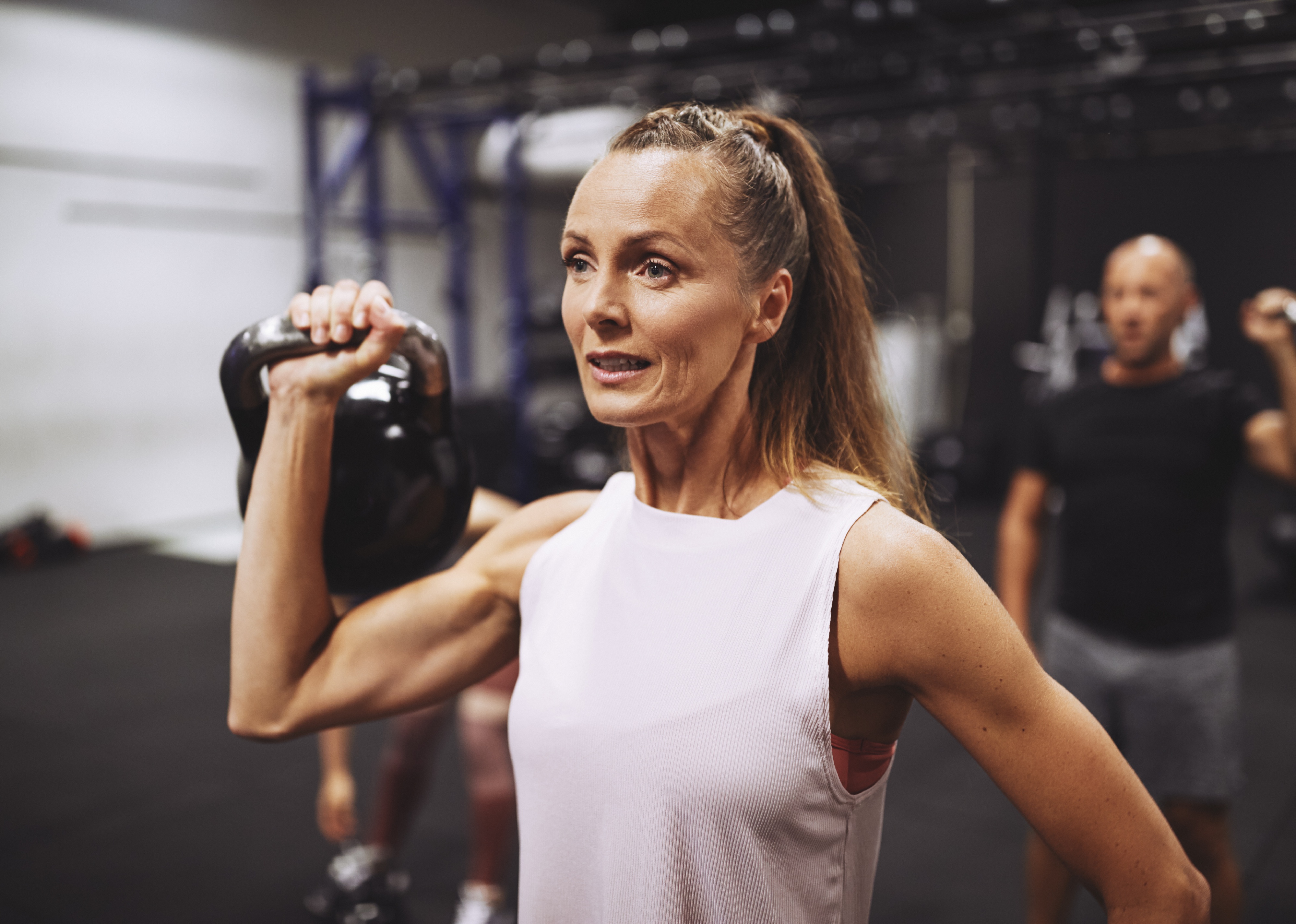 Woman in sportswear lifting a dumbbell during a strength training session at a gym.