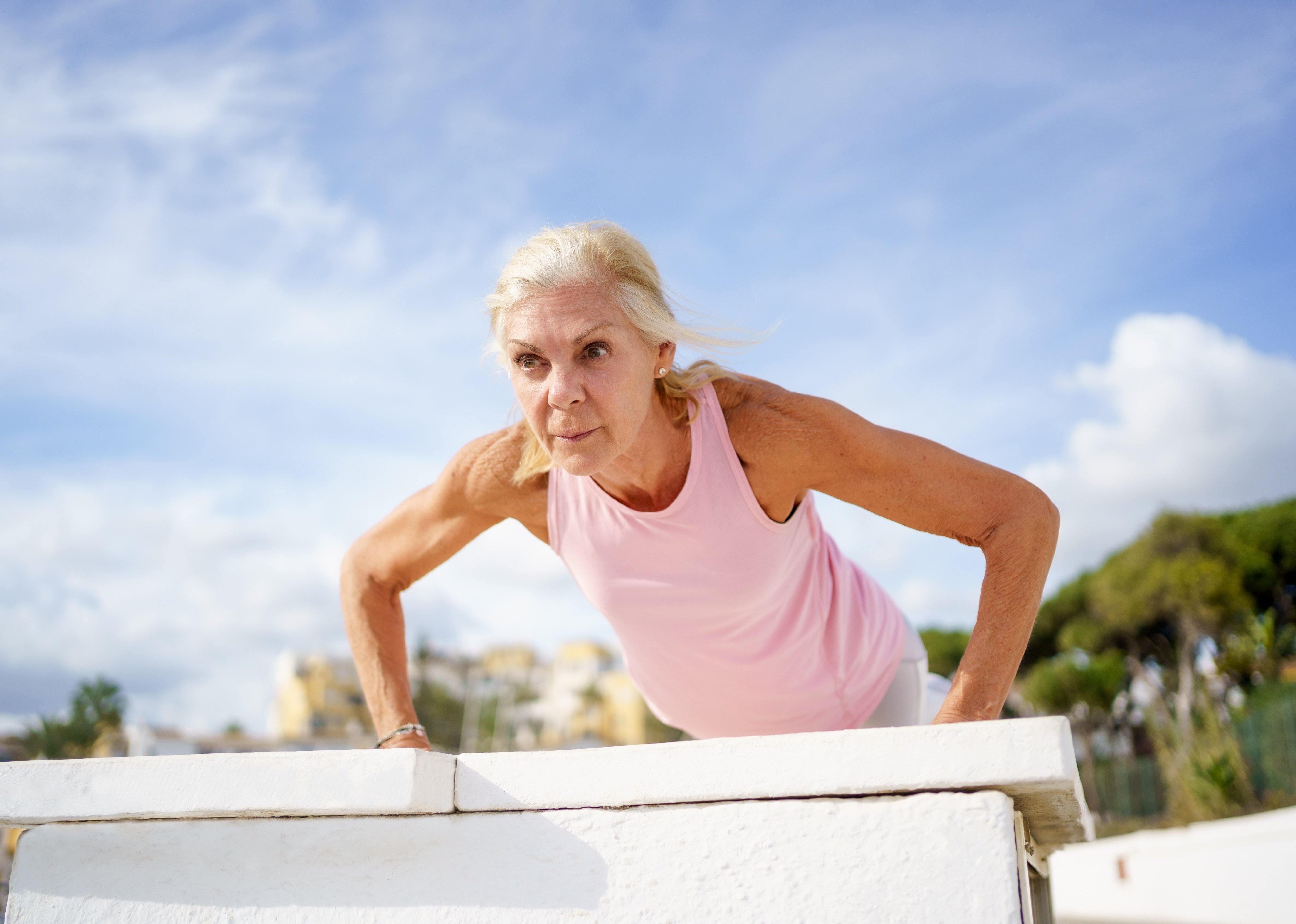 Senior female doing push ups outside with a blue sky behind her.