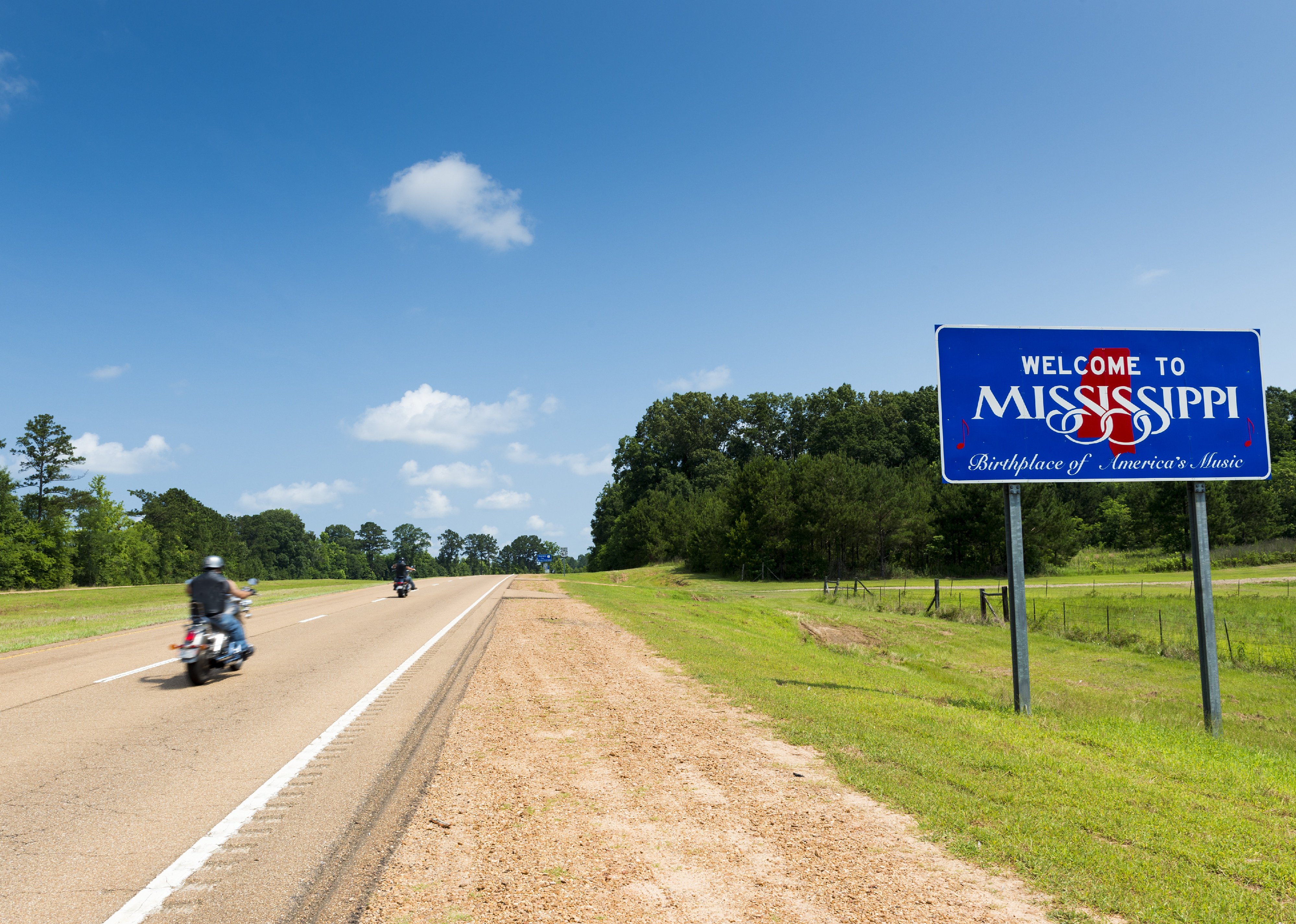 Two motorcycles passing by the Mississippi State welcome sign.