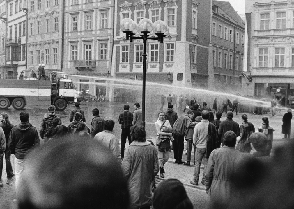 Trucks spray high-powered water hoses at protestors in the street as crowds gather.