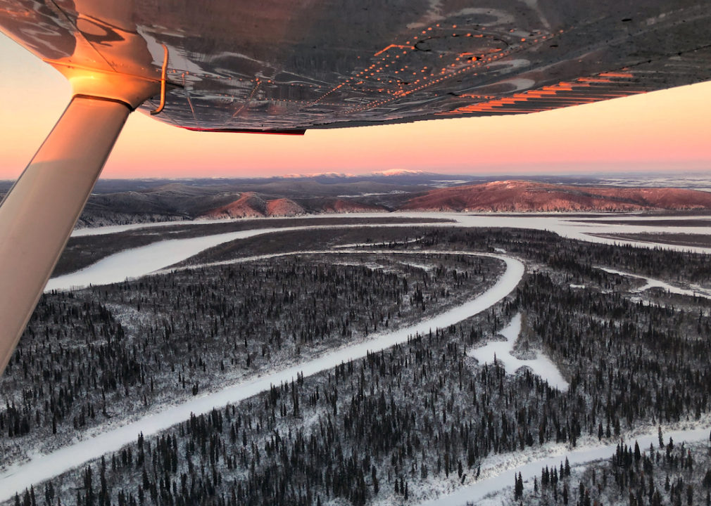 A snowy landscape view from a plane at sunrise.