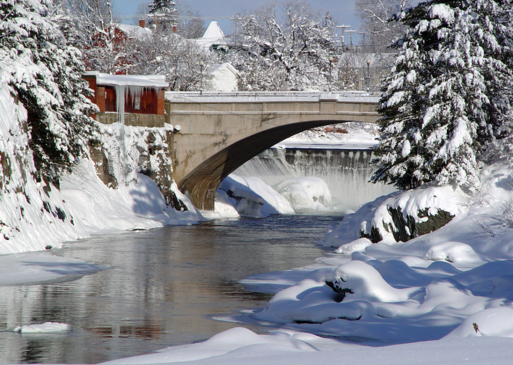 A frozen snowy bridge over a narrow river. 