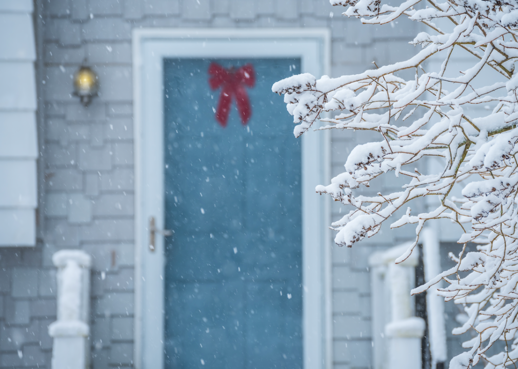 Snow falling on a tree with a decorated door in the background.