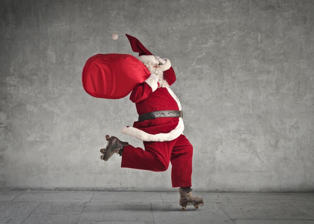 A roller skating Santa Claus carrying a red bag over his shoulder.