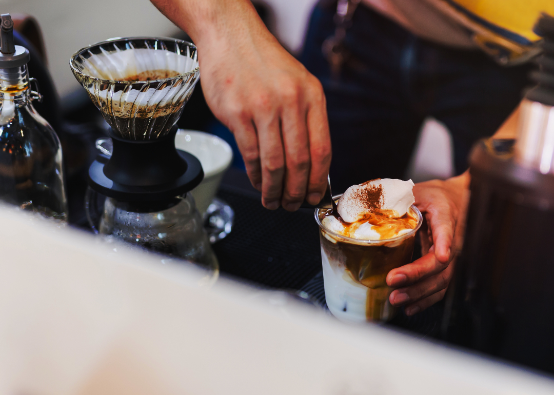 Close-up of barista pouring shot into coffee glass.