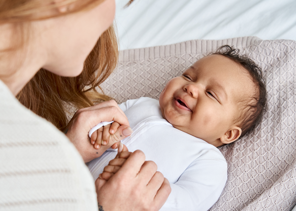 Mother holding smiling infant’s hands.