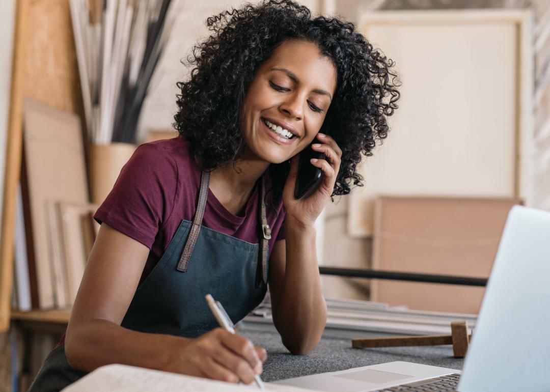 Small business owner speaking on phone taking notes.