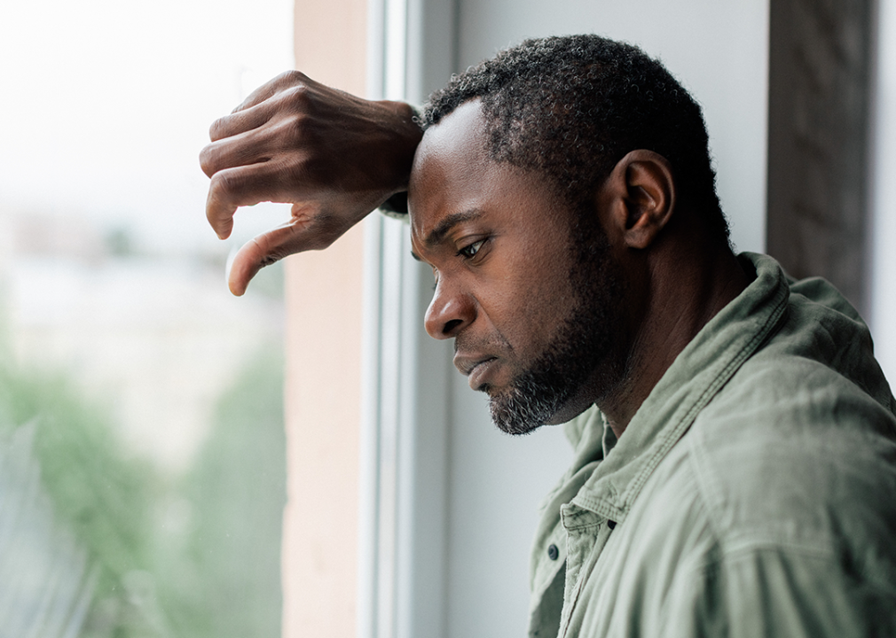 A sad-looking man with graying hair looking out window.