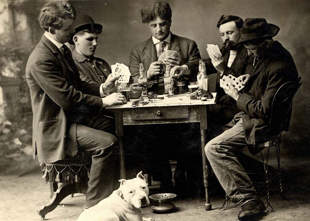 A black and white 1909 photo of five men playing poker around a table.