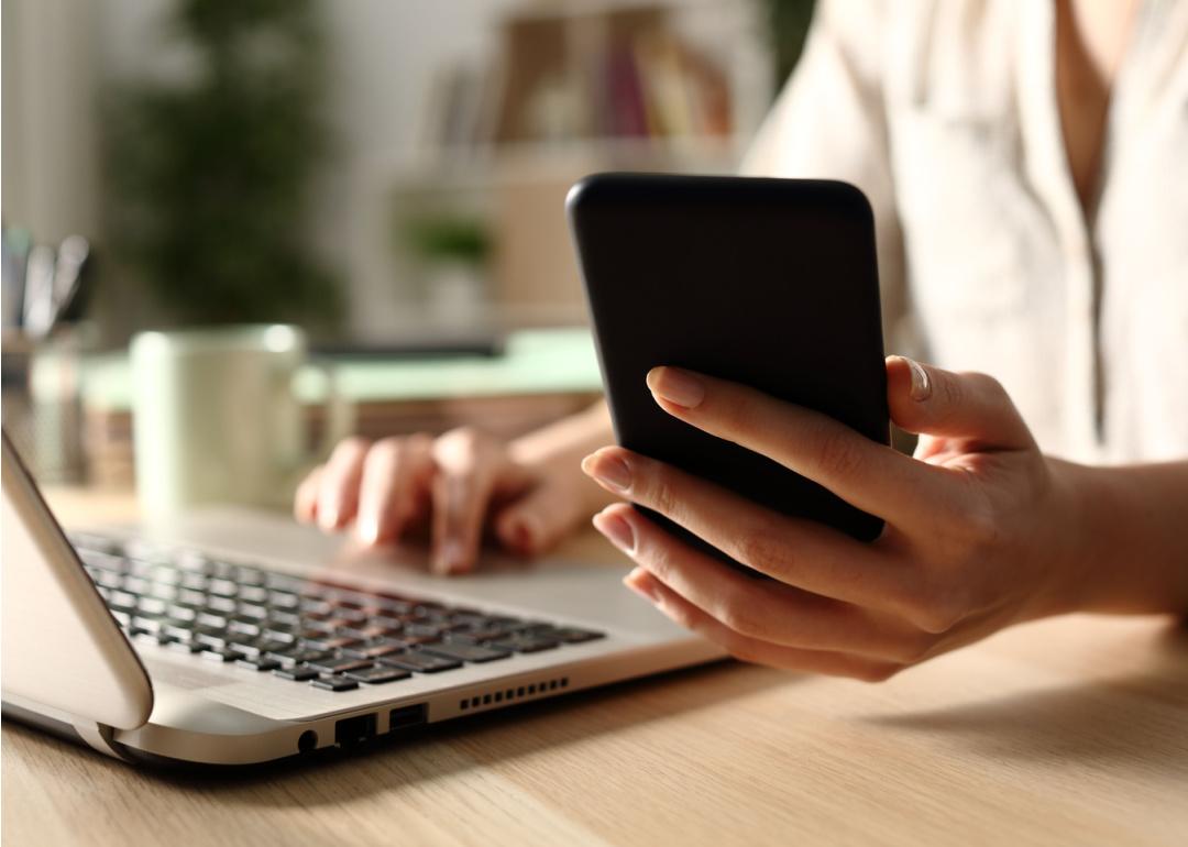 Woman using laptop and checking phone.