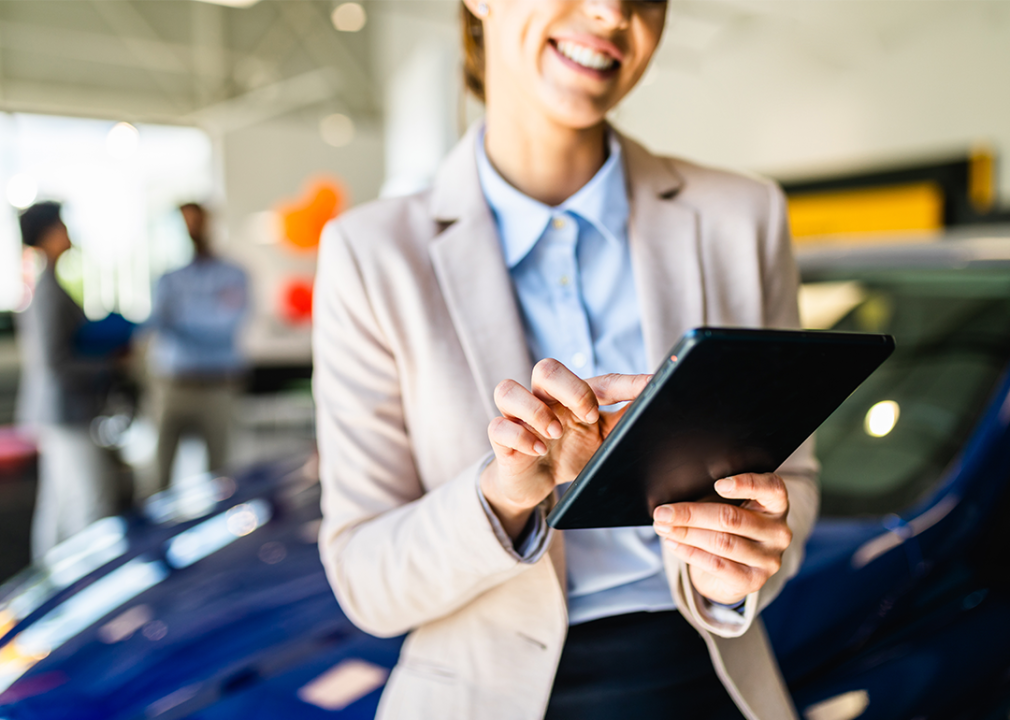 Woman in car dealership looking at tablet.