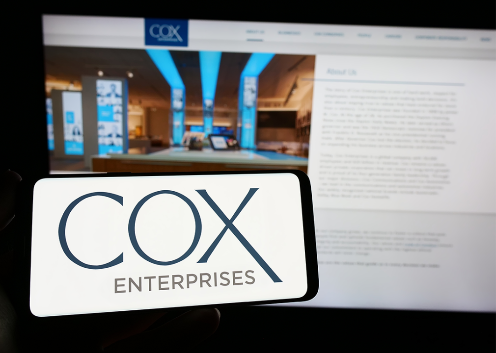 Phone with logo of Cox Enterprises Inc.on screen in front of website.