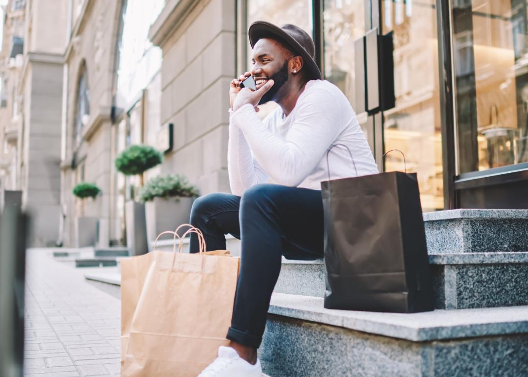 Smiling man in front of store with shopping bags holding phone