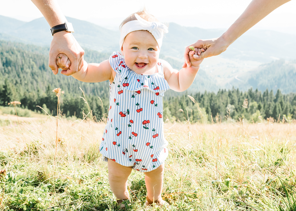 Parents holding toddler’s hand walking with mountain background.