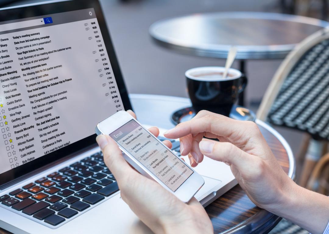 Person reading email on phone with laptop computer.