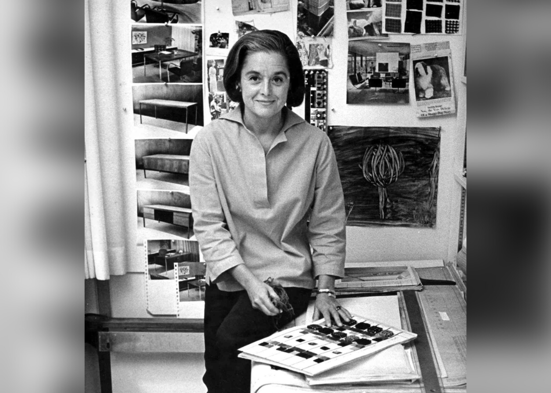 Florence Knoll Bassett sitting on table in studio with fabric swatches.