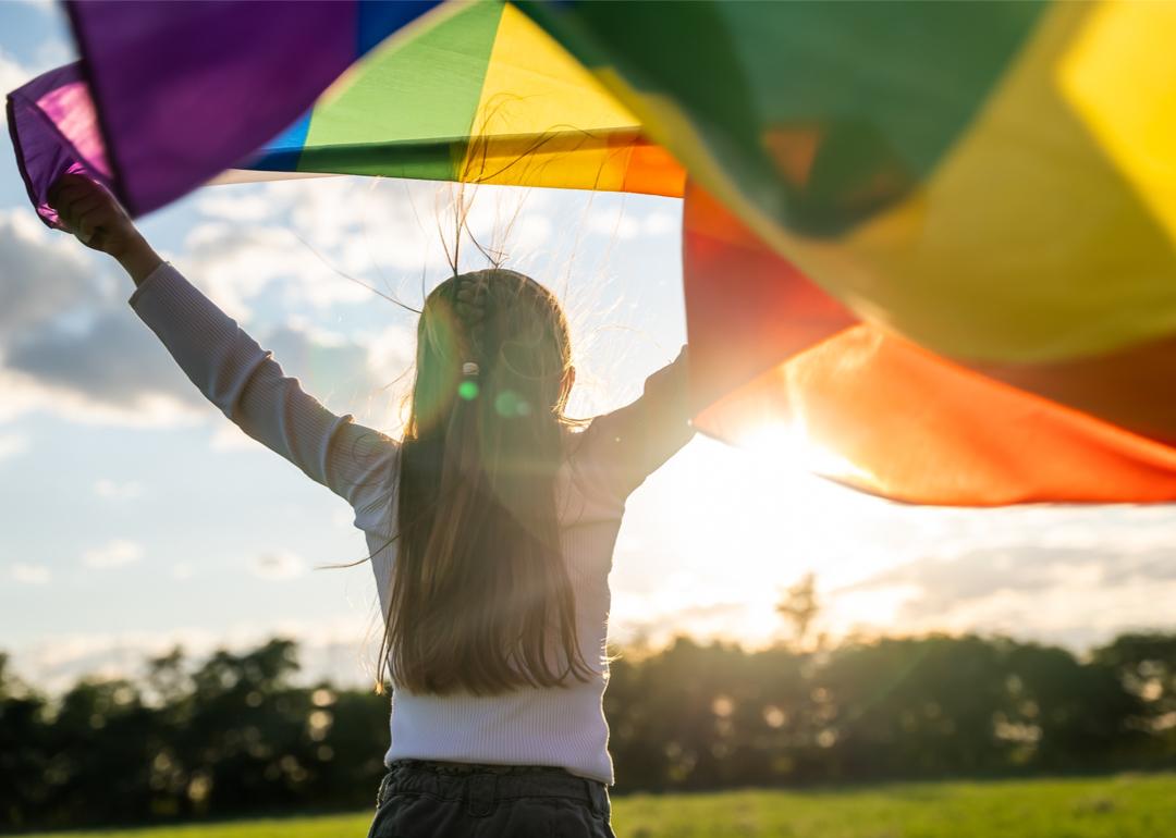 Child holding the rainbow flag against the blue sky.