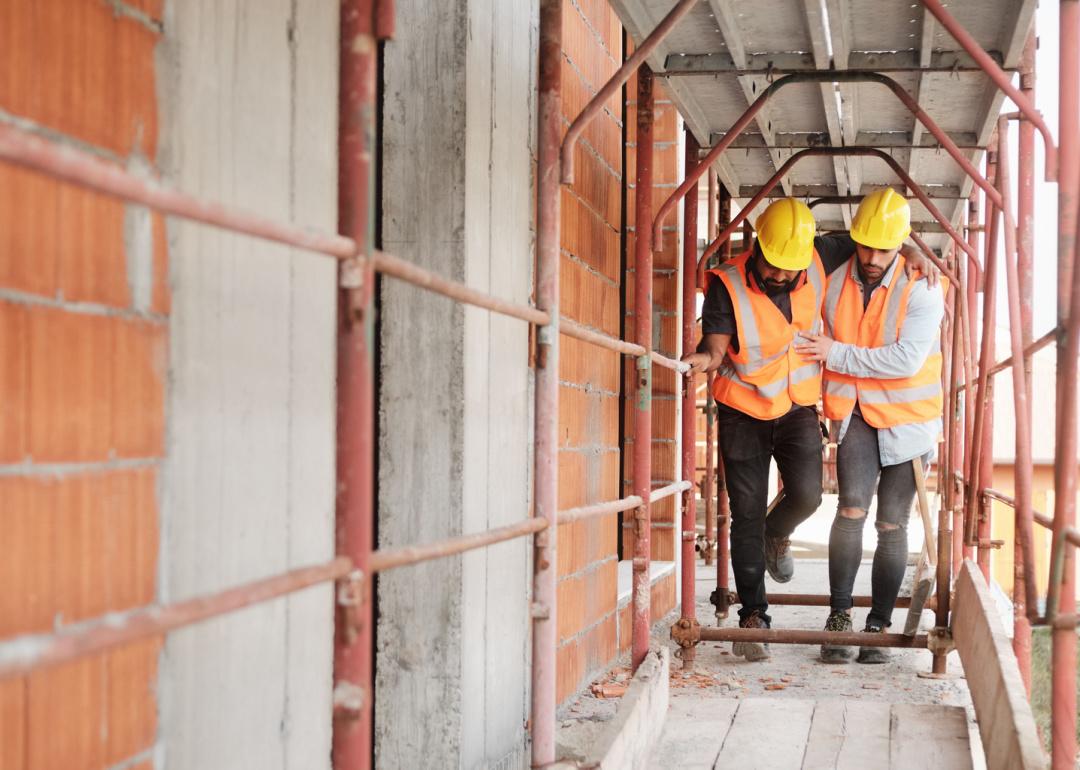 Construction worker helping injured coworker at job site.