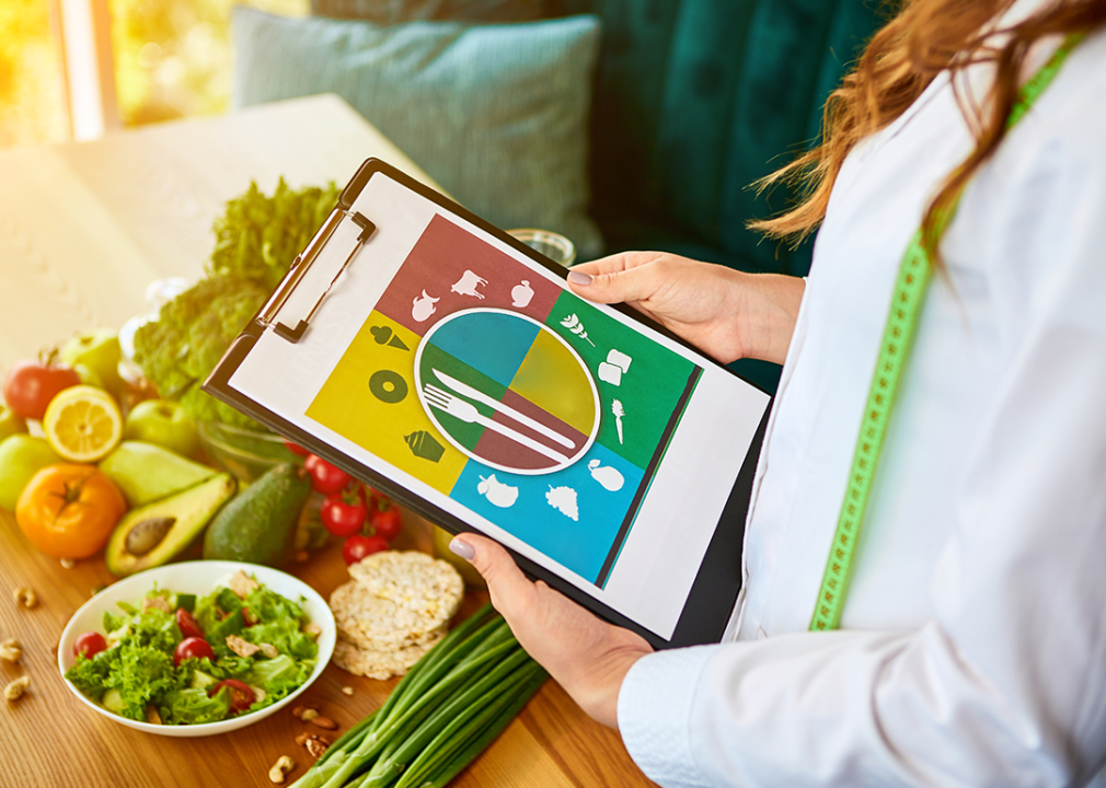 Nutritionist holding meal plan in front of a table full of healthy foods.