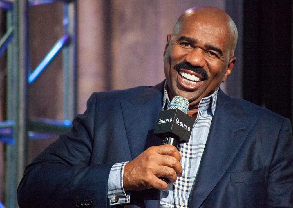 Steve Harvey holding microphone and smiling.